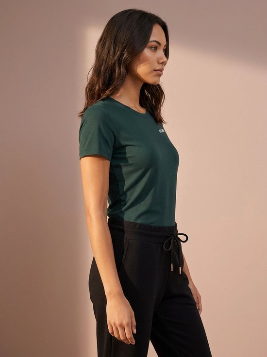 Model in donkergroen sportshirt met korte mouwen en wit SDS-logo, gecombineerd met zwarte joggingbroek.