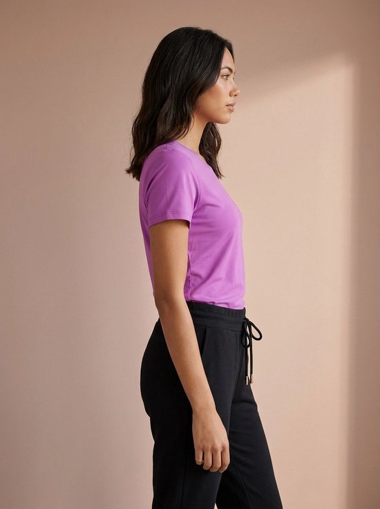 Zijaanzicht van vrouw in paars sportshirt met korte mouwen en zwarte sportbroek.