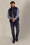 Man in donkerblauwe gewatteerde bodywarmer, blauw gebreid vest en jeans. Op de borst een Patch 'New Zealand Auckland'.