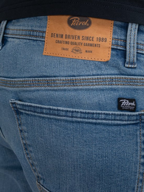 Detail van een blauwe spijkerbroek van Petrol Industries. Met lederen patch met 'Petrol, DENIM DRIVEN SINCE 1989' en klein logo.