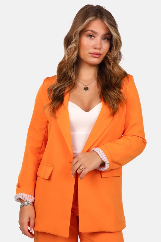 Close-up van het model in een oranje getailleerde blazer met opgerolde mouwen en witte top.