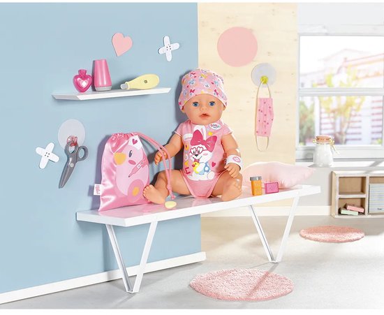 BABY born pop in roze outfit met konijnprint en mutsje, inclusief EHBO-accessoires en roze tasje op een bankje.