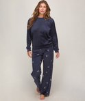 Model draagt een marineblauwe velours pyjamaset met een effen trui en een broek met een wit strikjespatroon.