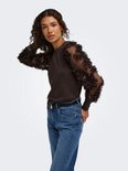 Model in bruine trui met doorschijnende mouwen met bloemapplicaties en jeans.
