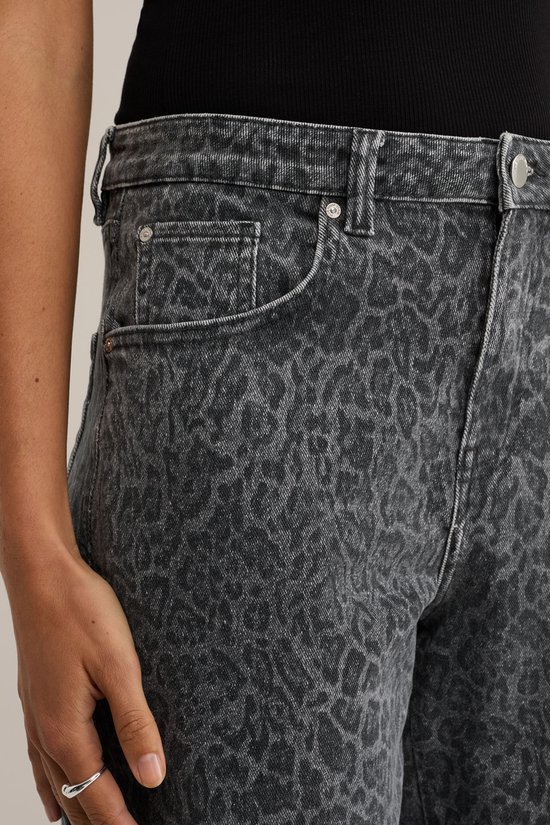 Close-up van een grijze jeans met luipaardprint. De broek heeft steekzakken aan de voorkant.