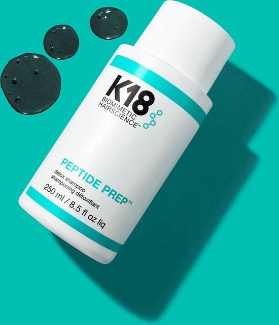 Witte K18 fles met turquoise accenten, naast donkere druppels. PEPTIDE PREP™ detox shampoo, 250 ml.