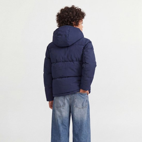 Achterkant van een jongen in een donkerblauwe pufferjas met capuchon en jeans.