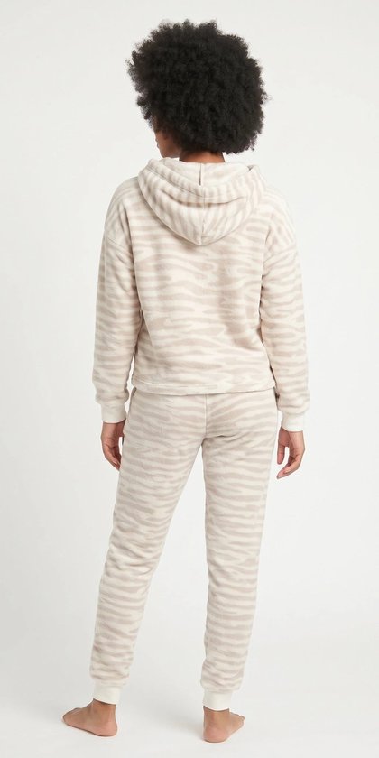 Model draagt de achterkant van beige fleece loungewear met zebraprint. De set bestaat uit een hoodie en een joggingbroek.