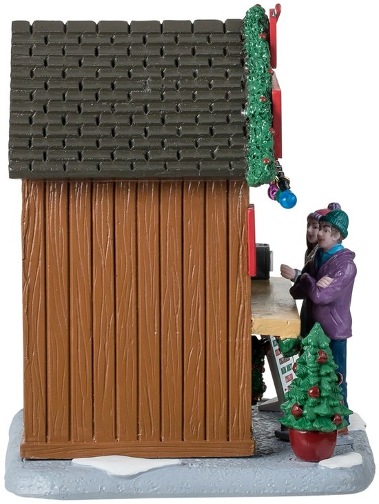 Zijaanzicht van een kerstkraam met een klant in een paarse jas en een kerstboom op een besneeuwde ondergrond.