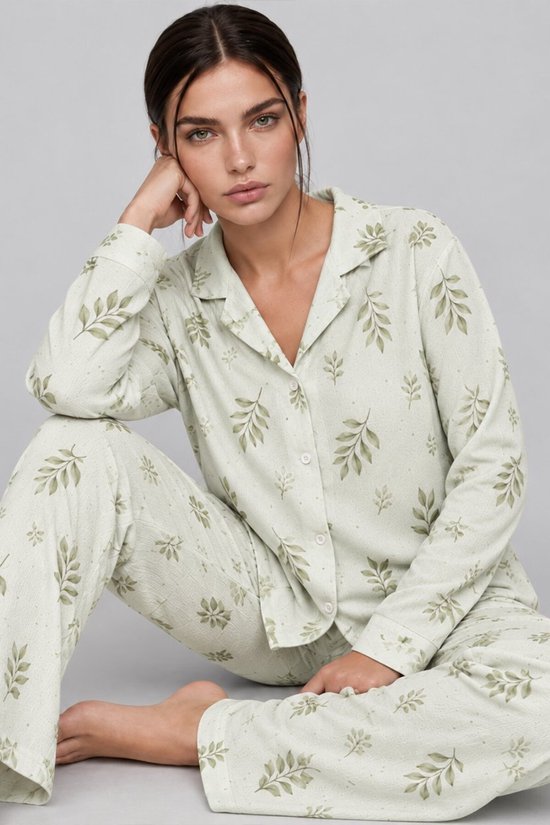 Model zit op de vloer in een saliegroene pyjamaset met bladerenprint en lange broek.