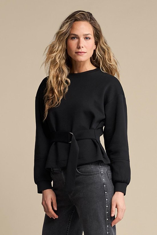 Model draagt zwarte sweater met ceintuur en jeans.