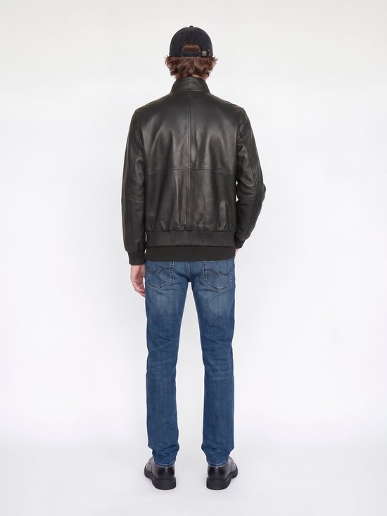 Rugaanzicht van een model in een zwarte leren jas, blauwe jeans en een pet.