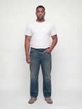 Man met korte mouwen wit T-shirt en blauwe relaxed fit jeans, handen in de zakken.