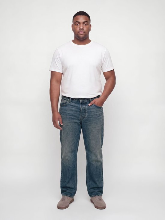 Man met korte mouwen wit T-shirt en blauwe relaxed fit jeans, handen in de zakken.