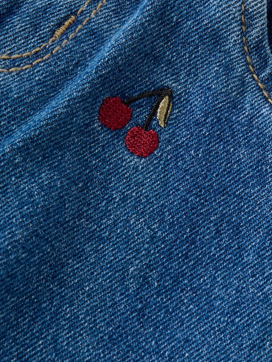 Detail van een kleine kersenborduursel op blauwe denimstof.