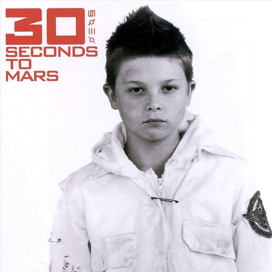 Jongen met kuif, witte jas met rits, kijkt ernstig naar de camera. Logo '30 Seconds To Mars' in rode letters.