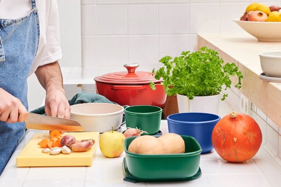 Plan de travail de cuisine avec des ingrédients pour la cuisine, y compris une cocotte rouge, des boîtes de conservation vertes et bleues et des légumes.