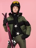 Meisje in ski-uitrusting, met groene pufferjas, helm, ski's en groene skibroek.