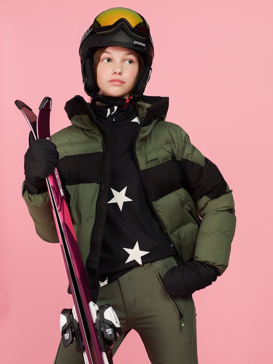 Meisje in ski-uitrusting, met groene pufferjas, helm, ski's en groene skibroek.