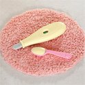 Gele thermometer en roze lepel met hartjesdetail op een roze vloerkleed.
