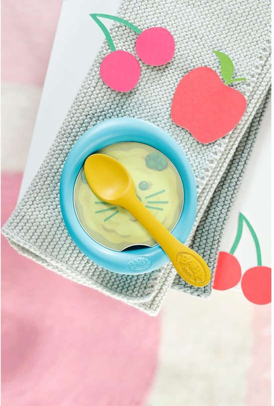 Blauw kommetje met eten en een gele lepel, versierd met papieren kersen en appel.