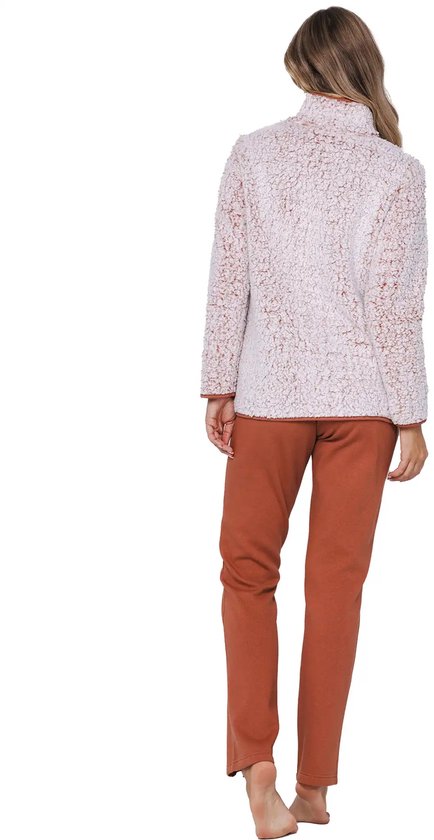 Vrouw staat in een lichtroze teddy fleece trui met bruine accenten en bijpassende broek.