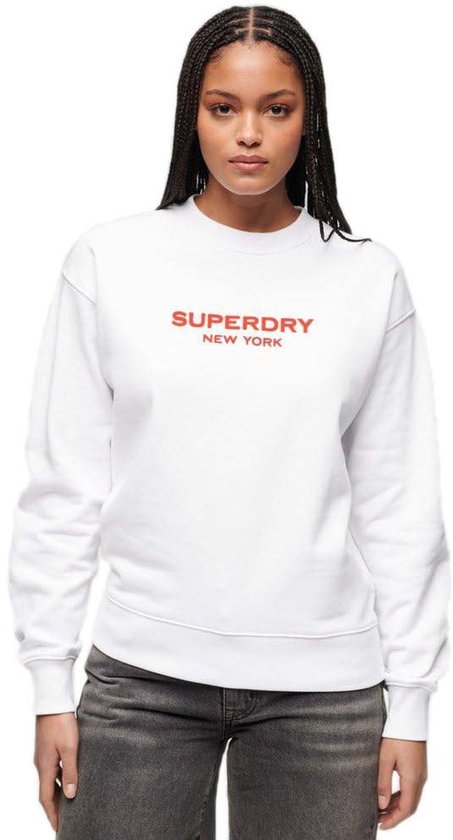Femme portant un sweat blanc avec l'inscription rouge "SUPERDRY NEW YORK".