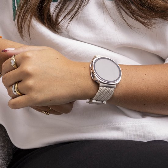 Een vrouw met een zilveren smartwatch met een beige stoffen band, ze draagt ringen.