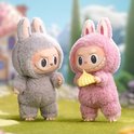 Twee Labubu macaron speelgoedfiguren in konijnenkostuums, één grijs, één roze die een geel gebakje vasthoudt.