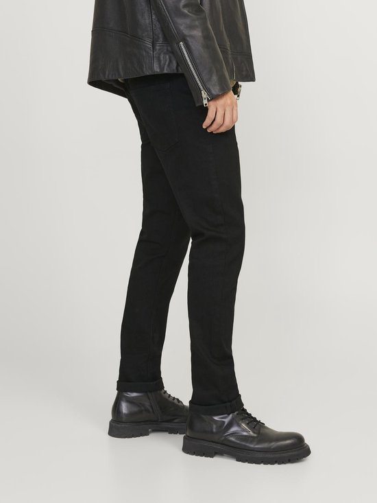 Man in zwarte jeans en zwart leren jack, staand, zijaanzicht.