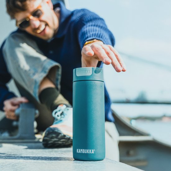 Man met zonnebril pakt een blauwe Kambukka thermosbeker aan.