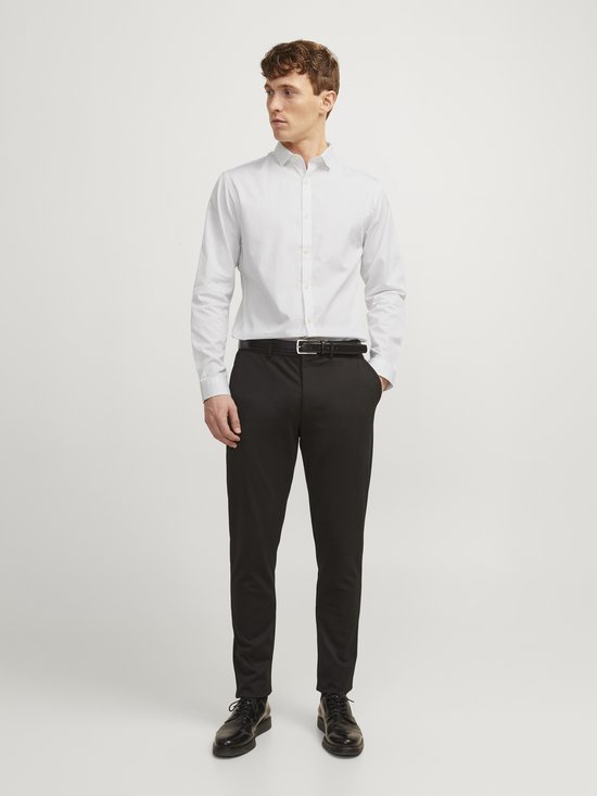 Man met wit overhemd en zwarte broek, met zwarte riem.