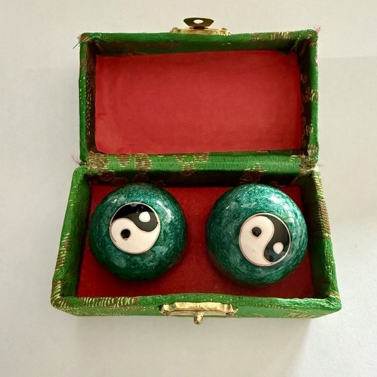 Twee ronde, groene meridiaankogels met een Yin Yang symbool, in een groene kist met rode voering.