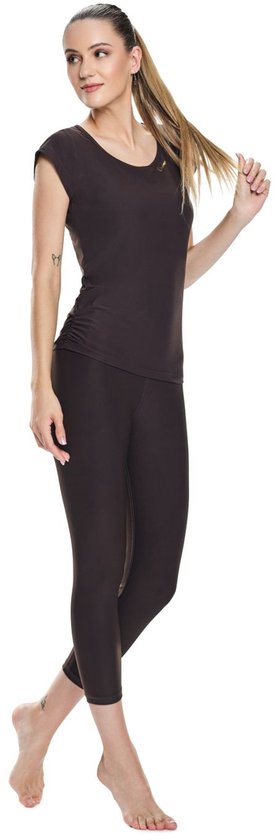 Model draagt een donkerbruin shirt met korte mouwen en een bijpassende driekwart legging. Ze speelt met haar haar.