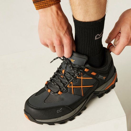 Handen die een man met zwarte sokken in een oranje-zwarte Regatta wandelschoen strikken.