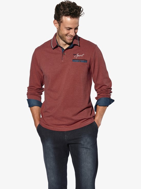 Man met rood langarm polo shirt met 'Free Spirit' borduring en denim zakje, gedragen met jeans.