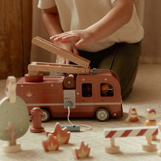 Kind speelt met houten brandweerwagen, ladder, poppetjes, boom, hydrant en vuurelementen.