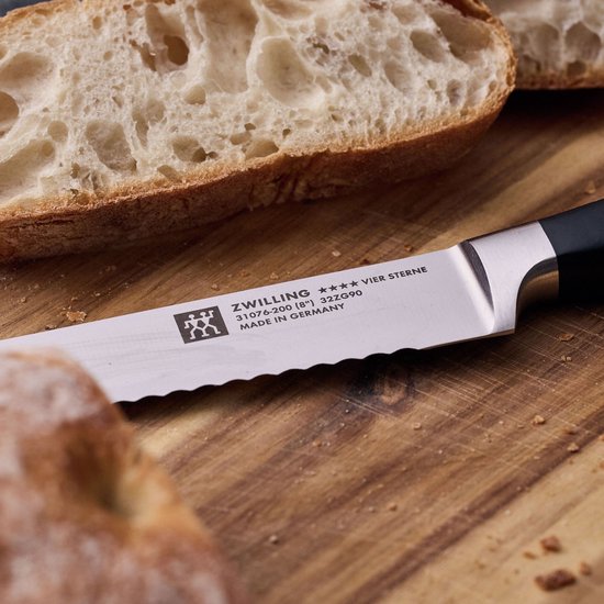 Gedetailleerde opname van een ZWILLING broodmes met kartelrand op een houten snijplank, naast gesneden brood.