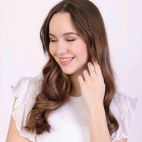 Een jonge vrouw met lang bruin haar draagt een zilverkleurige ring met zirkonia.