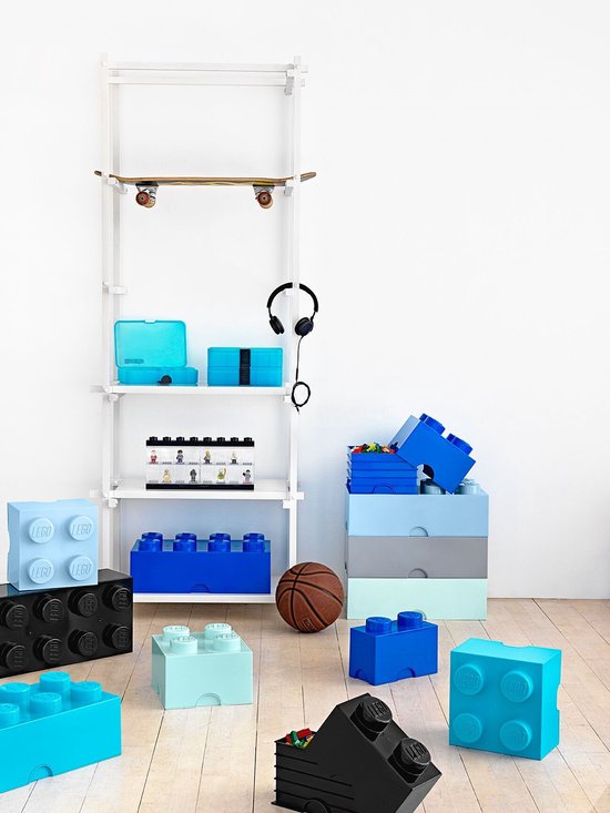 Chambre d'enfant moderne avec étagère blanche avec skateboard et casque, et diverses boîtes de rangement Lego bleues, bleu clair et noires au sol.