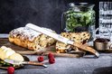 Glaceerd brood met rozijnen en amandelen, gesneden, met een broodmes met olijfhouten handvat en fruit.