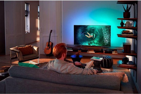 Man met rode baard kijkt naar een Philips tv met Ambilight en een duiker op het scherm.