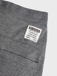 Close-up van het label op een donkergrijze joggingbroek met tekst: 'NMT 028-65196 LOOK UP & GET LOST 2 THE MOON & BACK SPECIAL EDITION CREATED TO IMPRESS ITEM NO.: 028/6'.