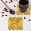 Deux sous-verres dorés à motif de Noël blanc, à côté d'une tasse de café et de grains de café.