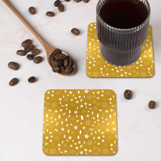 Deux sous-verres dorés à motif de Noël blanc, à côté d'une tasse de café et de grains de café.