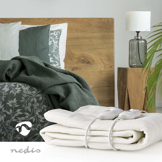 Witte elektrische deken met twee bedieningselementen, opgemaakt op een bed met houten hoofdeinde.