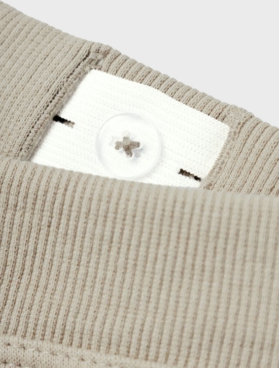 Detail van de tailleband van een grijze joggingbroek met knoopsluiting.