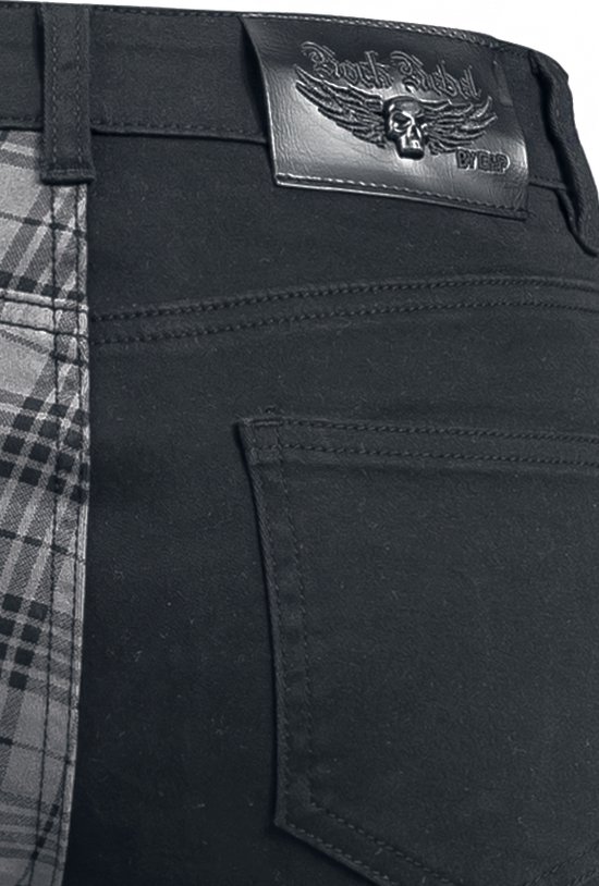 Detail van de achterkant van een broek met een zwart leren label met doodshoofd en vleugels. De broek is zwart met een vak rechts.