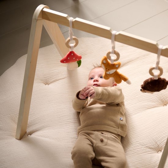 Baby liggend onder een babygym met paddestoel, vos en egel speelgoedjes.