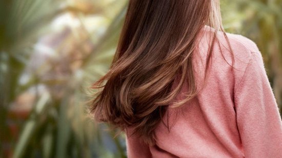 Achterkant van een vrouw met lang, bruin, golvend haar, gedragen in de wind.